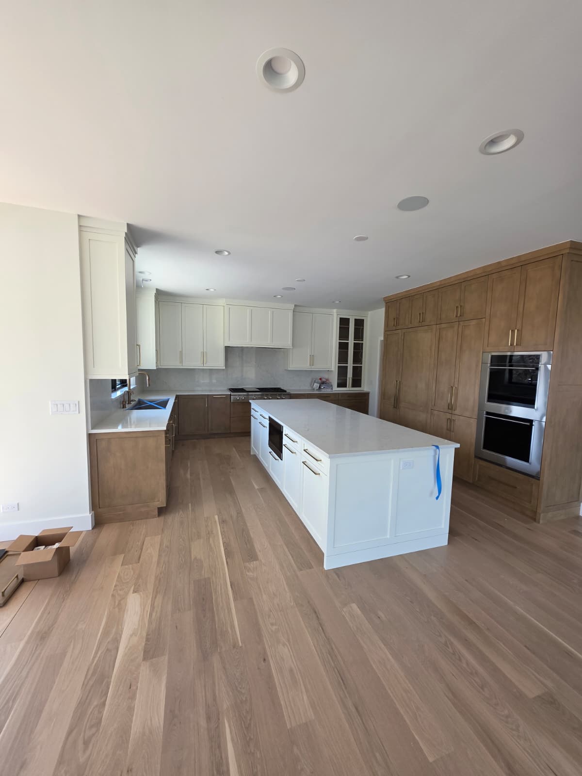 Kitchen with a long quartz island, painted and stained cabinetry and integrated wall ovens