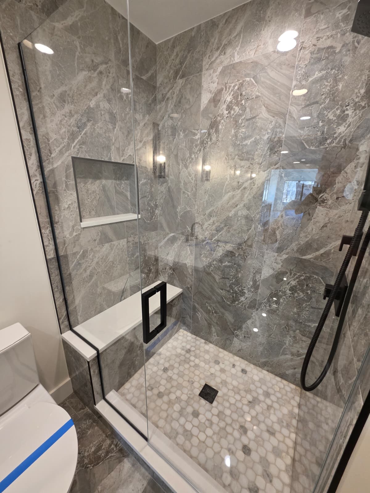 Walk-in shower clad in large-format grey marble tile with hex mosaic floor and black fixtures