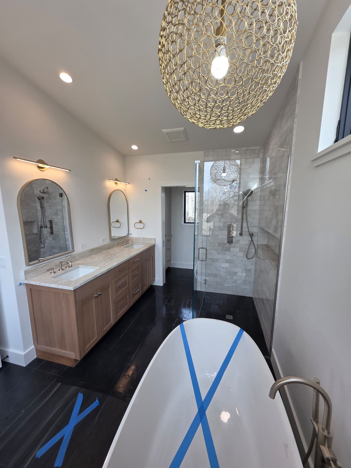 Primary bath suite with white oak vanity, arched mirrors and a sculptural brass pendant
