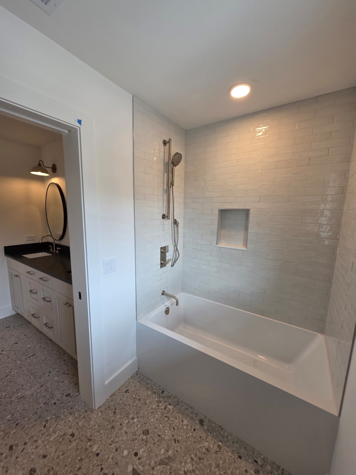 Bathroom with a tiled tub and shower surround, niche and terrazzo-style flooring