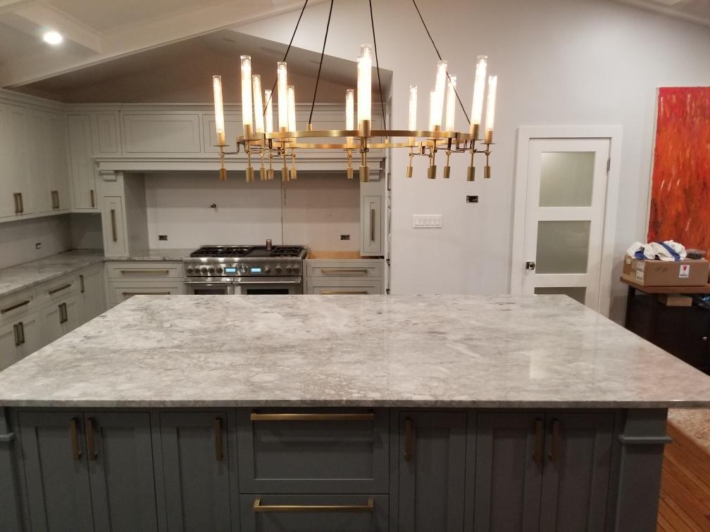 Kitchen with a large marble-look island, grey cabinetry and a linear brass chandelier