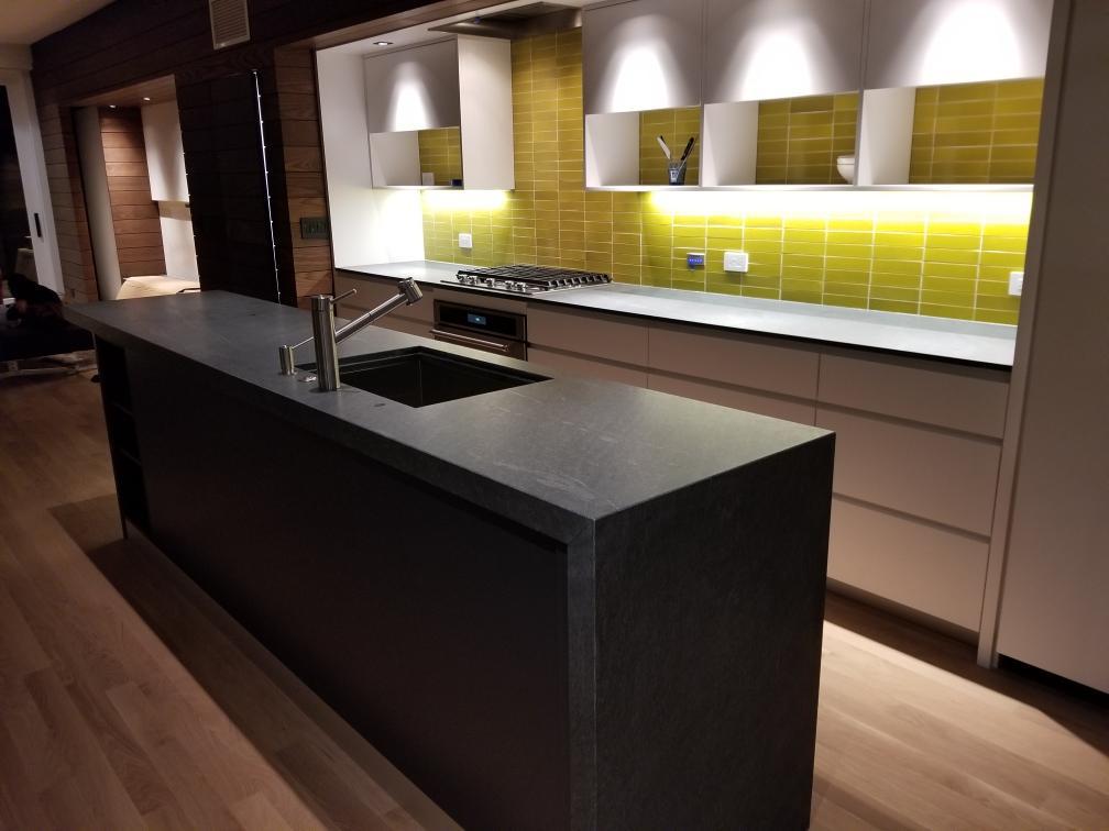 Modern kitchen with a long dark stone island, handleless cabinetry and lit glass tile backsplash