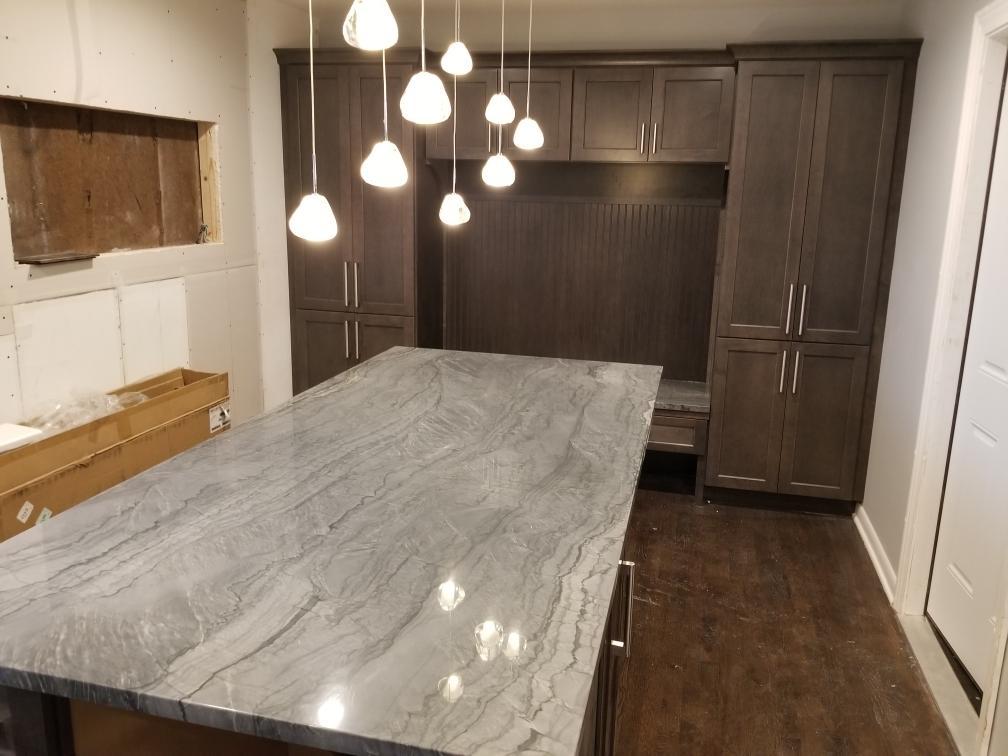 Veined stone island with espresso-stained cabinetry and a cluster of pendant lights