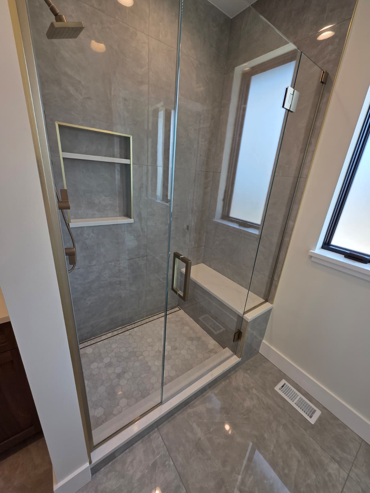 Walk-in shower with large-format stone tile, a built-in bench, niche and frameless glass