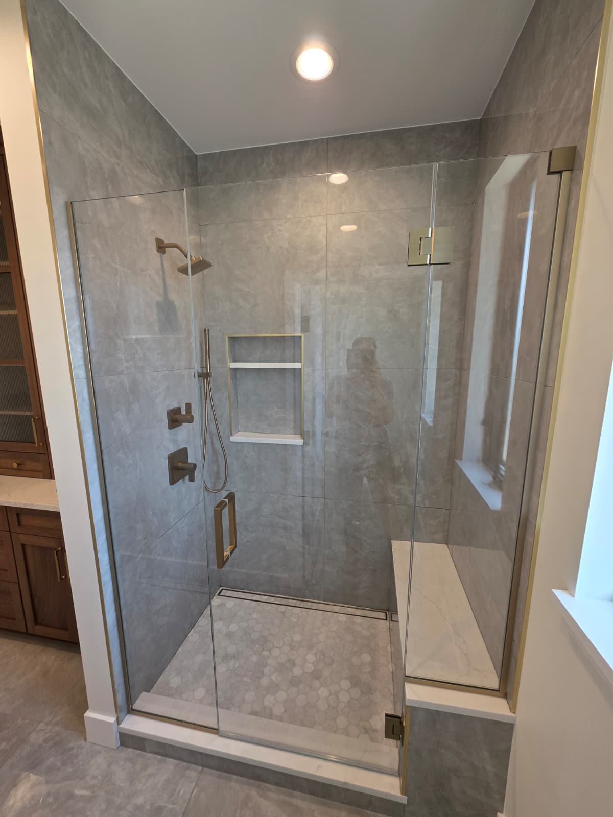Frameless glass shower enclosure with grey stone tile, hex mosaic floor and brass hardware