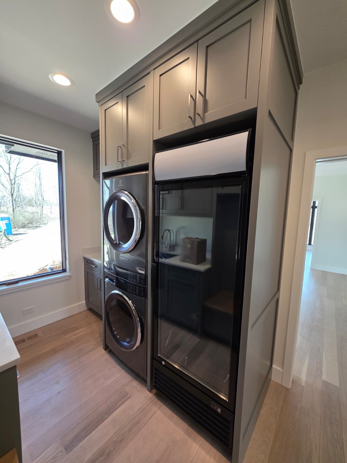 Laundry room with built-in painted cabinetry, stacked washer and dryer and integrated refrigeration